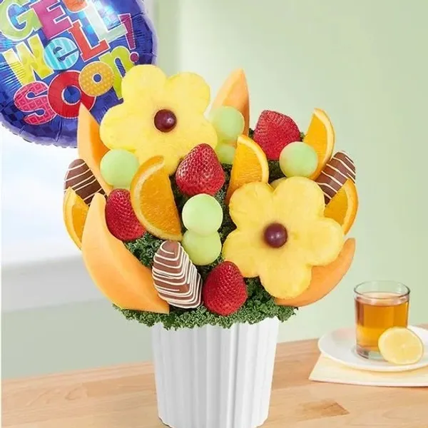 A fruit bouquet arranged in a white pot, featuring pineapple flowers, strawberries, cantaloupe slice 