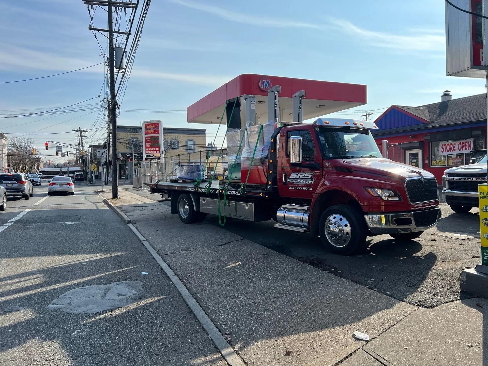 SRS Towing & Recovery’s red flatbed tow truck carrying a red and white gas station canopy, secured with straps, in an urban area.