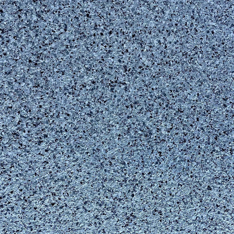 A close-up, top-down view of a textured surface composed of small, irregularly shaped chips in varying shades of gray and black, set against a lighter blue-gray background.