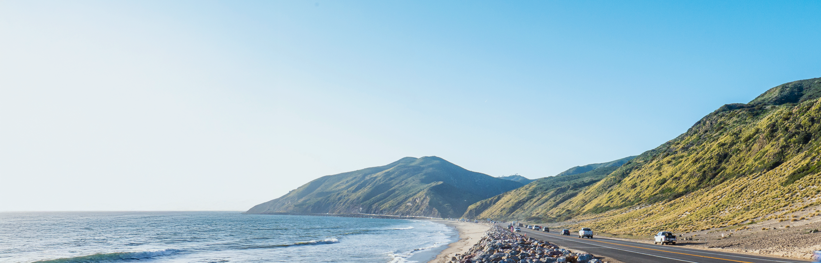 A seaside highway bordering mountains on the right and an ocean to the left.