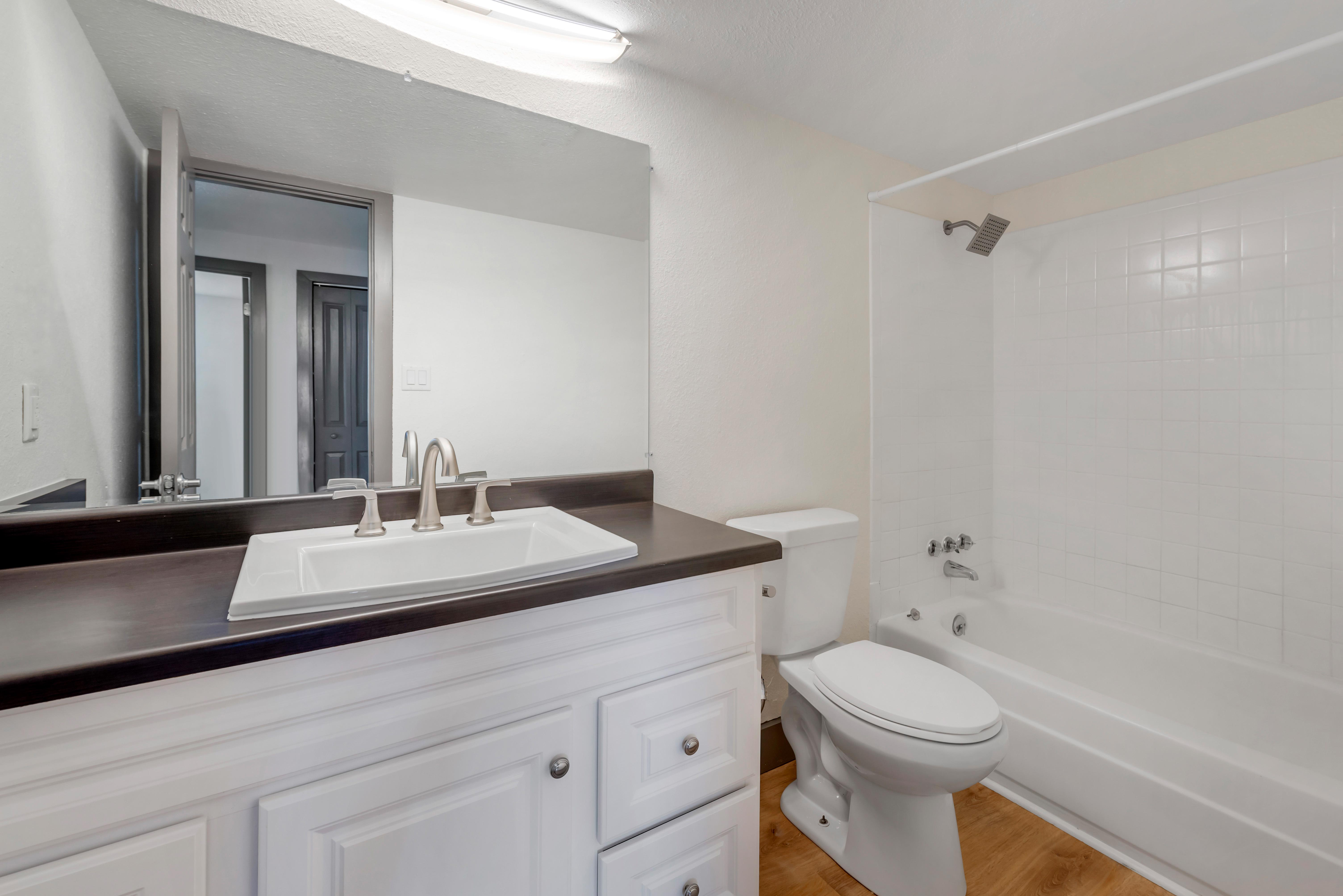 Vinyl floored bathroom with white cabinets, shower/bathtub combination, and modern hardware.