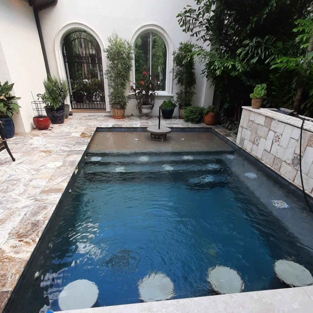 Compact courtyard swimming pool with dark blue water, stone decking, decorative fountain features, and lush landscaping.