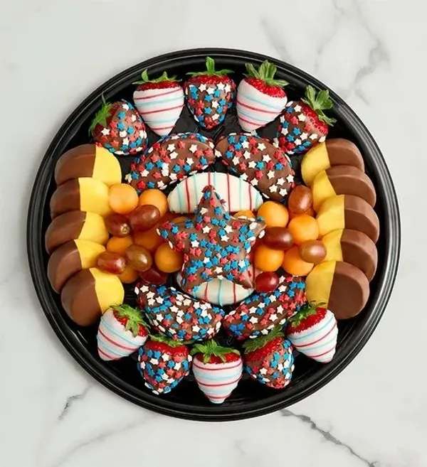 A patriotic fruit platter arranged on a black tray. The platter features chocolate-dipped strawberri 