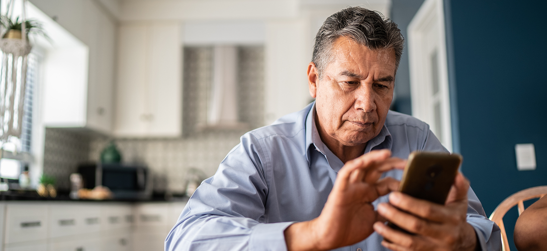 An older gentlemen on his phone at the kitchen table.