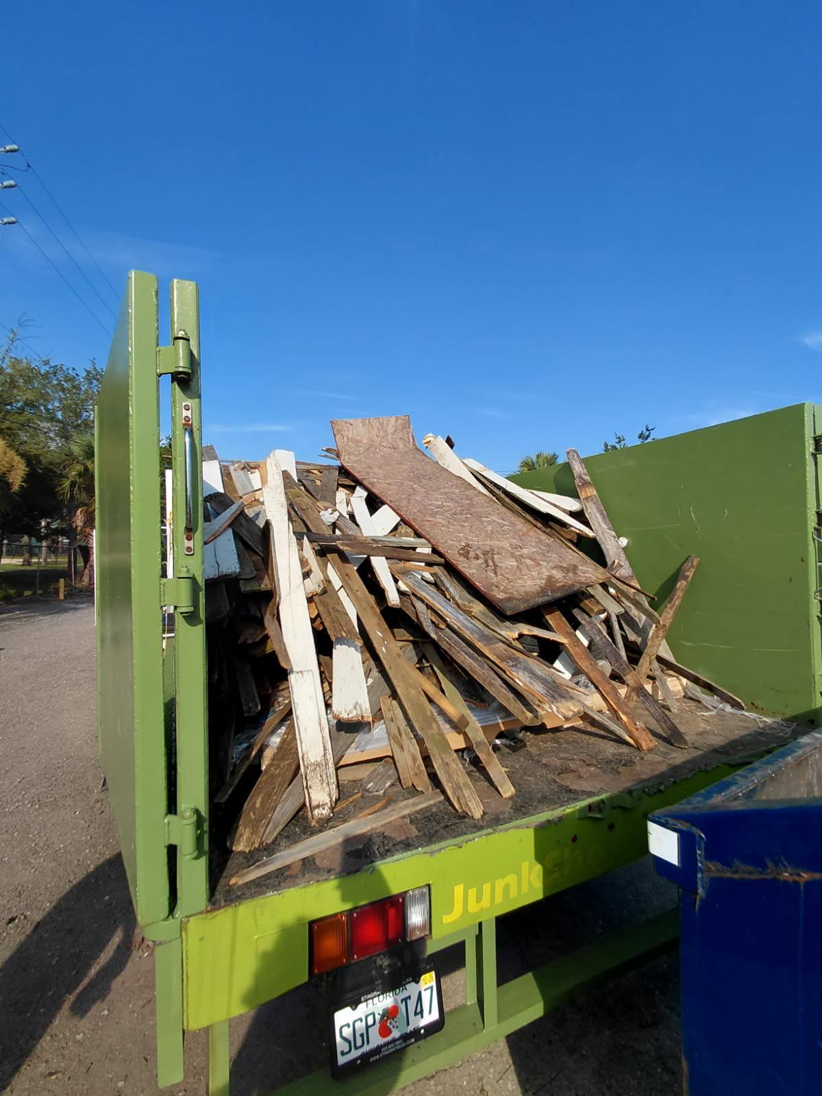 The open back of a green JunkShot truck loaded with scrap wood, plywood sheets, and timber framing. 