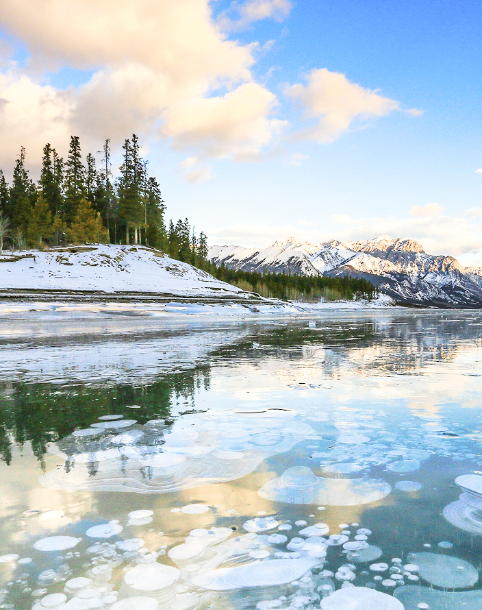 An icy lake leading to a rugged, snow-capped mountain range.