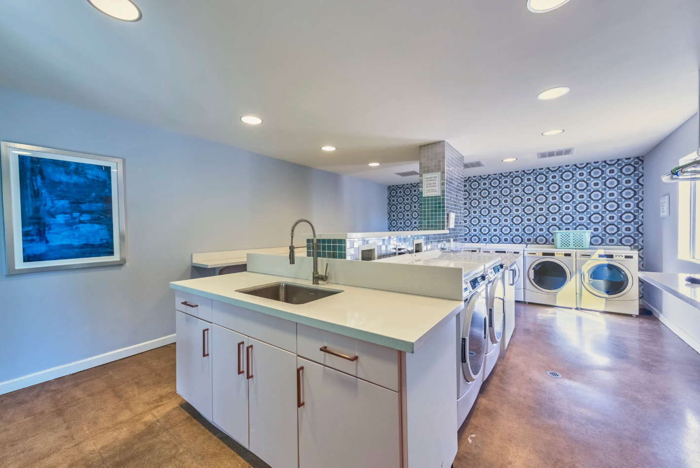 Resident Laundry Facilities with Multiple Washers and Dryers, a Tile Patterned Wall, and a sink with White Cabinetry