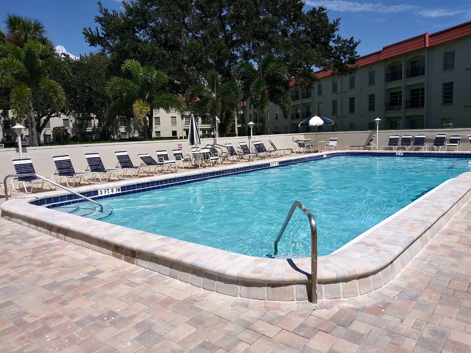 Large community swimming pool with surrounding paver deck, safety handrails, and lounge seating.