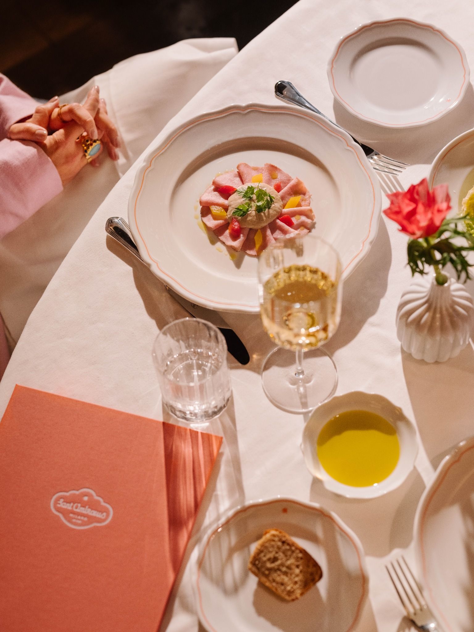 Overhead view of a fine-dining table with a plated appetizer, white wine, bread, and elegant tableware.