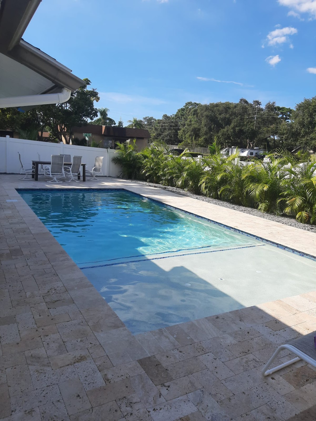 Modern rectangular backyard pool with a shallow sun shelf, clear blue water, light stone decking, and landscaped surroundings.