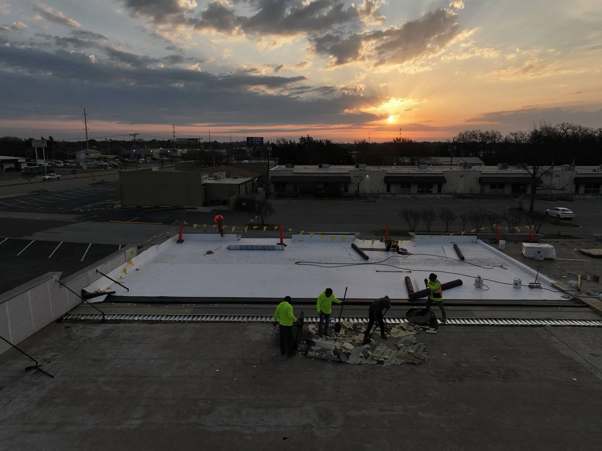 Commercial roofing crew installing a new flat roofing system during sunset, demonstrating profession 