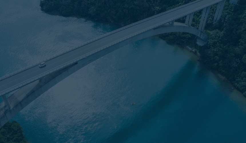A modern concrete bridge crossing over turquoise water in a forested area.