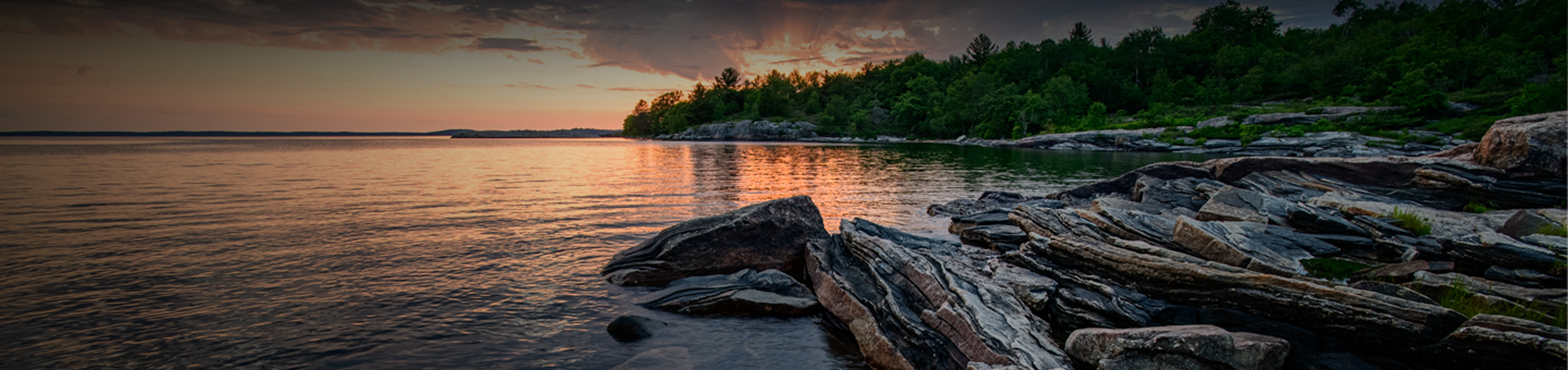 Close up of a rocky shore and calm water at sunset.