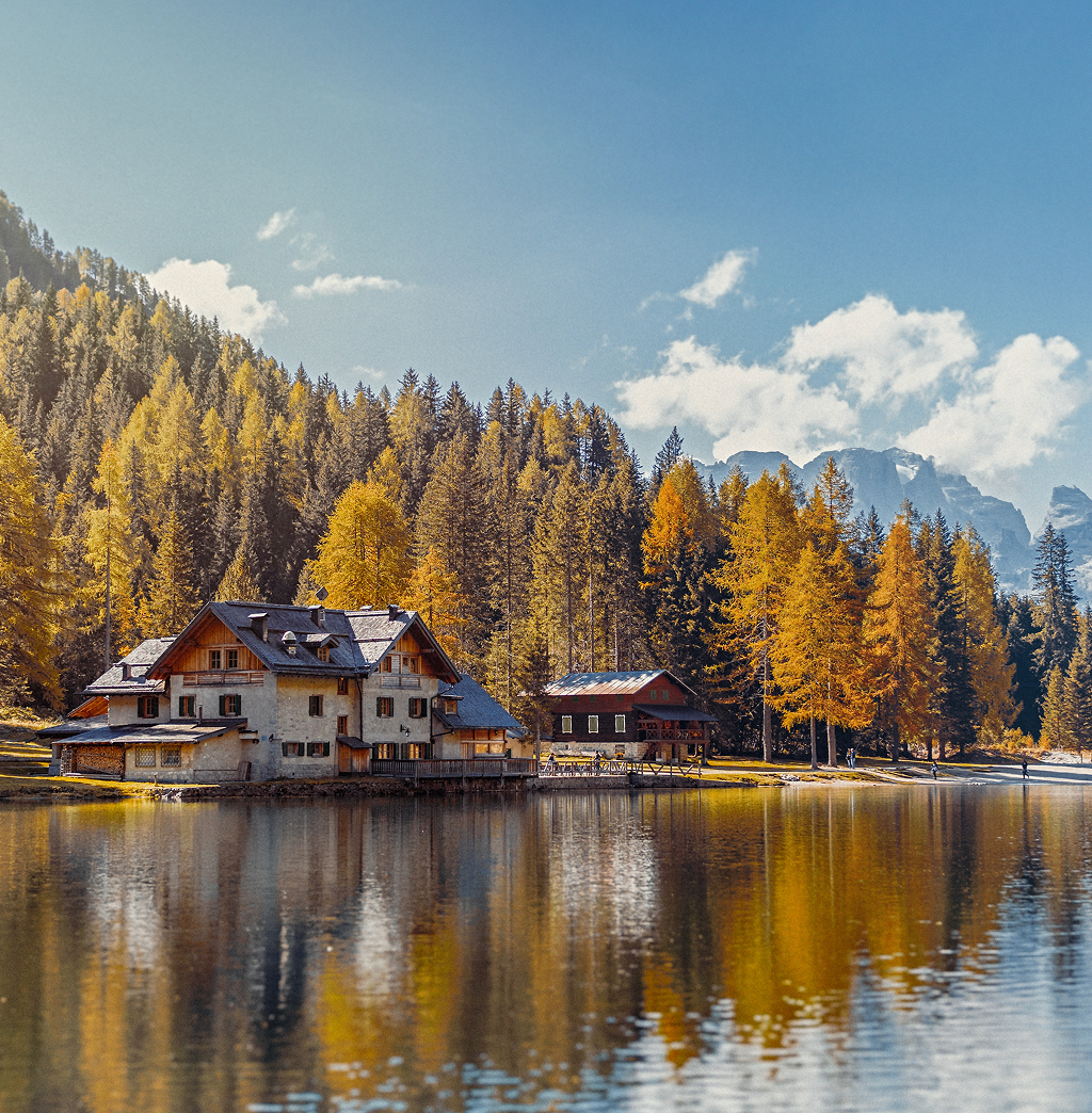 Gorgeous lakeside cottage surrounded by multicoloured fall trees and mountains in the background.