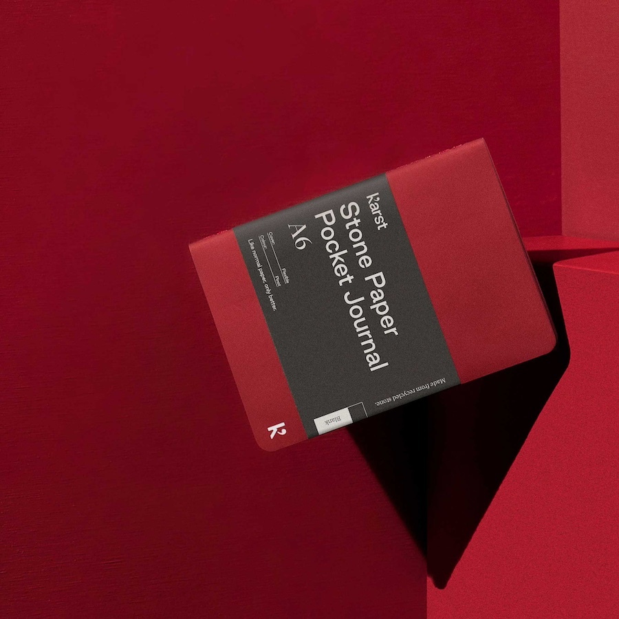 A minimalist product image by Tabula Rasa Social Stationers, featuring a red Karst Stone Paper Pocket Journal in A6 size. This journal highlights Karst's innovative, eco-friendly paper, crafted entirely from sustainably sourced recycled stone, offering a silky-smooth, tear-resistant, and waterproof writing experience. The product's clean design and vibrant red hue are showcased against a matching red geometric backdrop, emphasizing its modern aesthetic and commitment to sustainability.