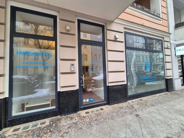 Praxis für Osteopathie am Ludwigkirchplatz & Heilpraktiker für Psychotherapie Außenansicht der Praxisräume mit Schaufenstern, zeigt den Standort für Osteopathie, Psychotherapie und systemische Therapie