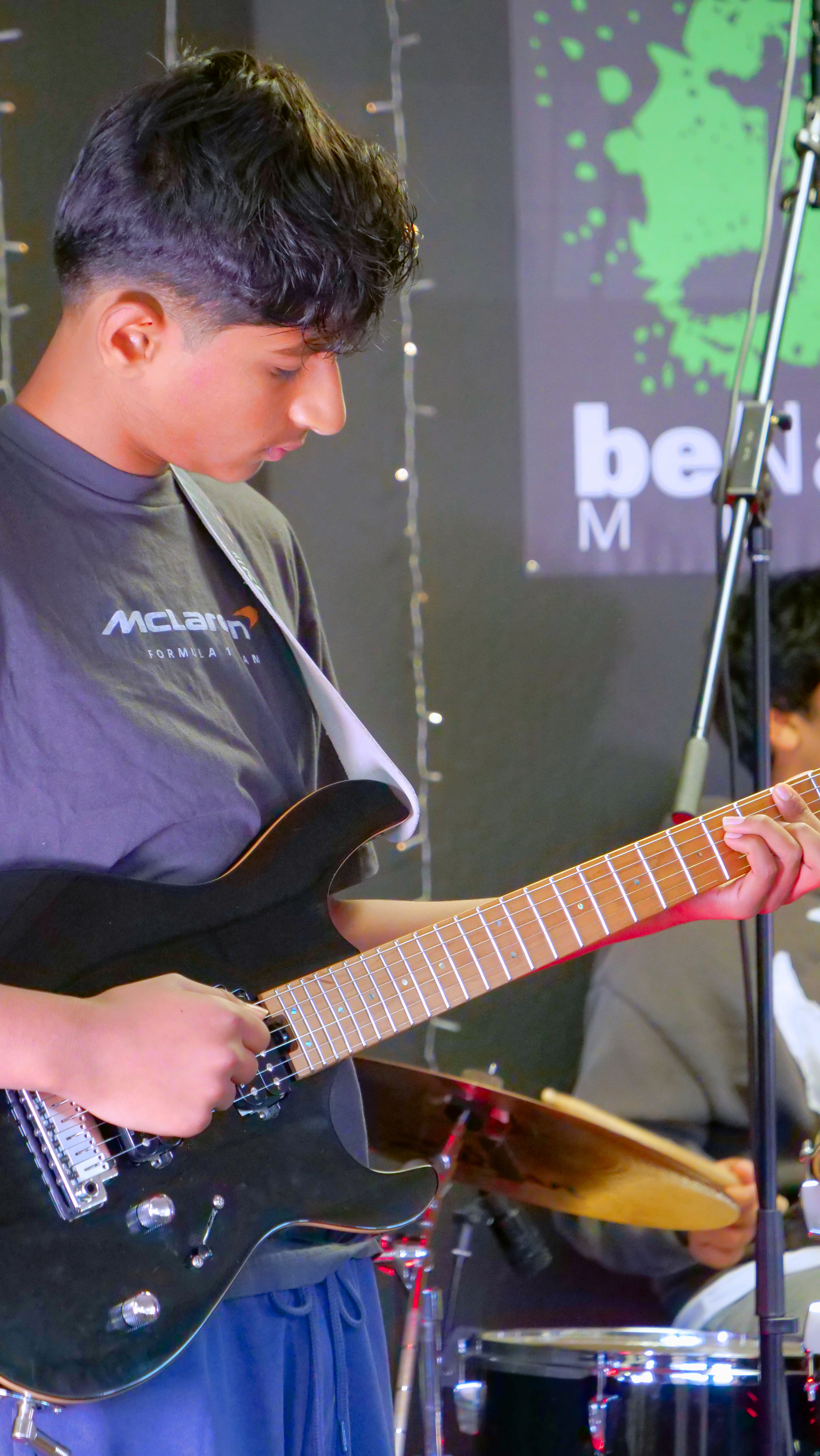 Student guitarist performing on stage during a live music performance program.