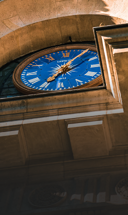 Blue clock on the outside of a historic building.