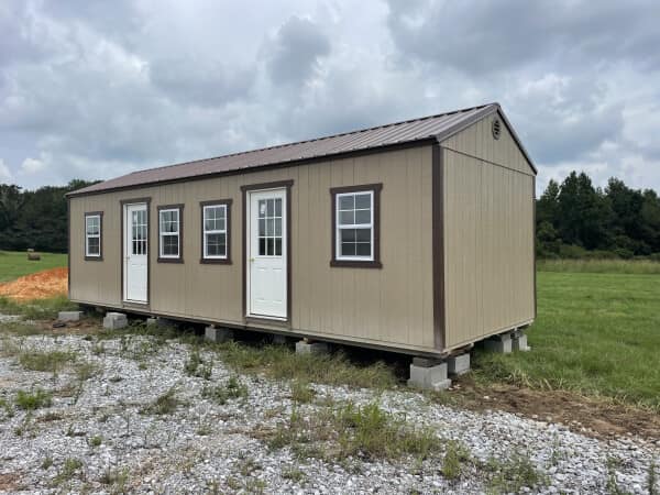Tan portable office building elevated on concrete blocks featuring dual entry doors, multiple windows, and brown trim. Designed for offices, classrooms, or flexible workspace applications in outdoor settings.
