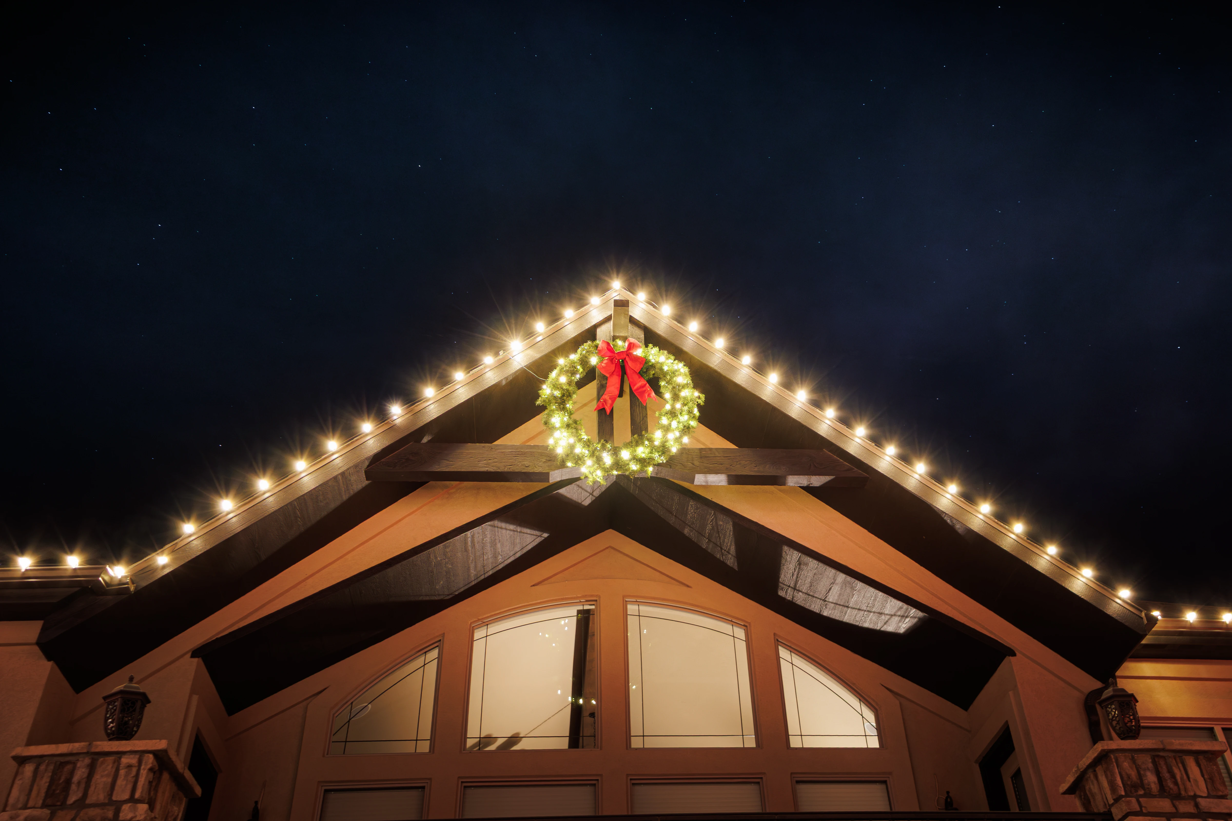 Lights follow the gable line to the peak, with a lit wreath centred on the truss. 