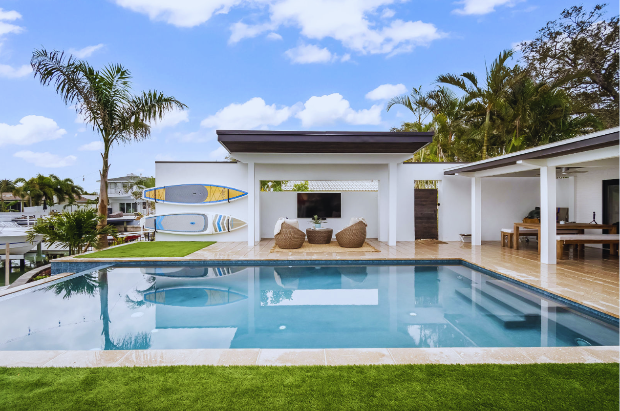 Contemporary waterfront swimming pool with clear blue water, a covered outdoor living area, and tropical landscaping.