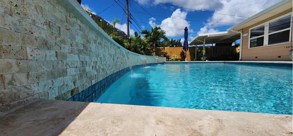 Custom backyard pool featuring clear blue water, stone accents, and a modern outdoor entertaining area.
