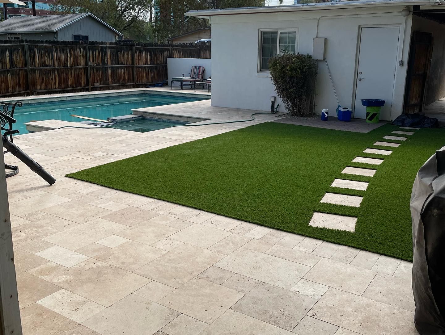 A backyard with a clean patio, a swimming pool, and artificial turf featuring a stepping stone path to a white building.