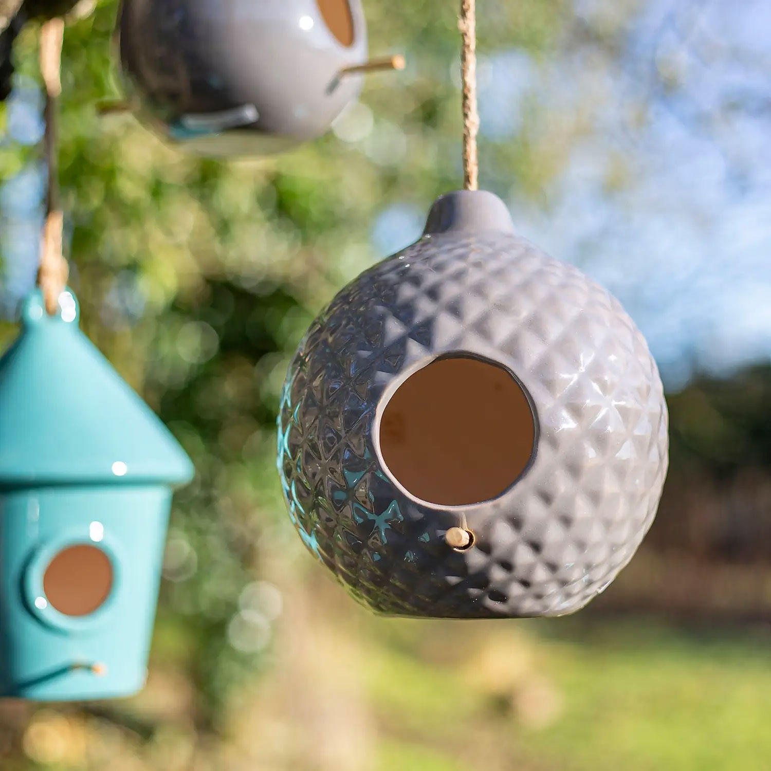 Three modern bird feeders hanging in a garden