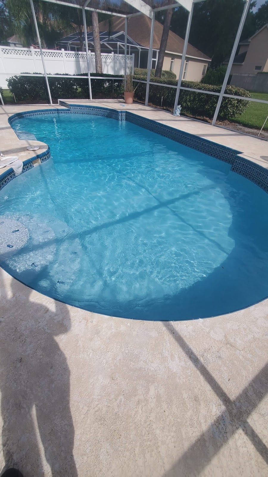 Screen-enclosed residential pool with clear blue water, curved edges, and a spacious concrete pool deck.