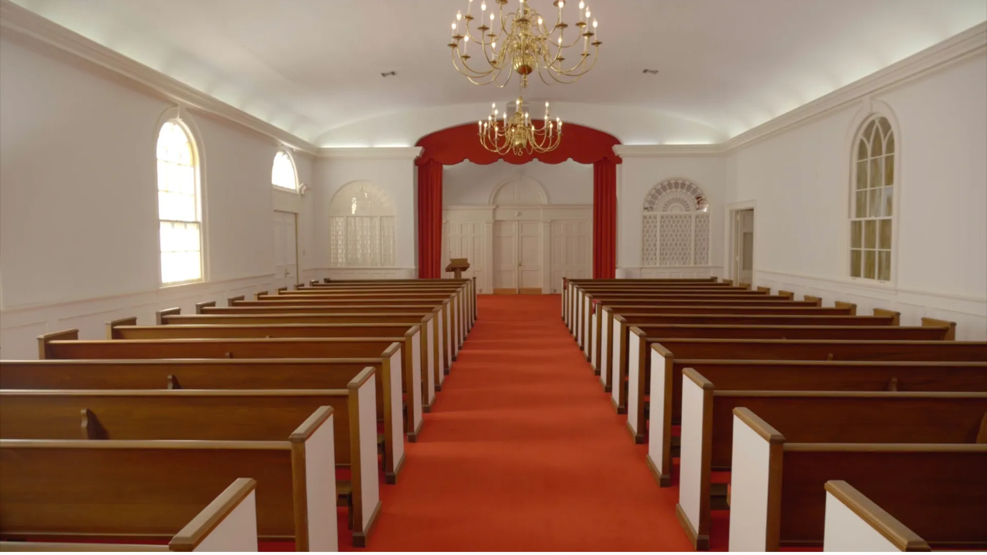 Platt's Augusta chapel, with rows of wood pews, a red carpet aisle, and crystal chandeliers, set up  