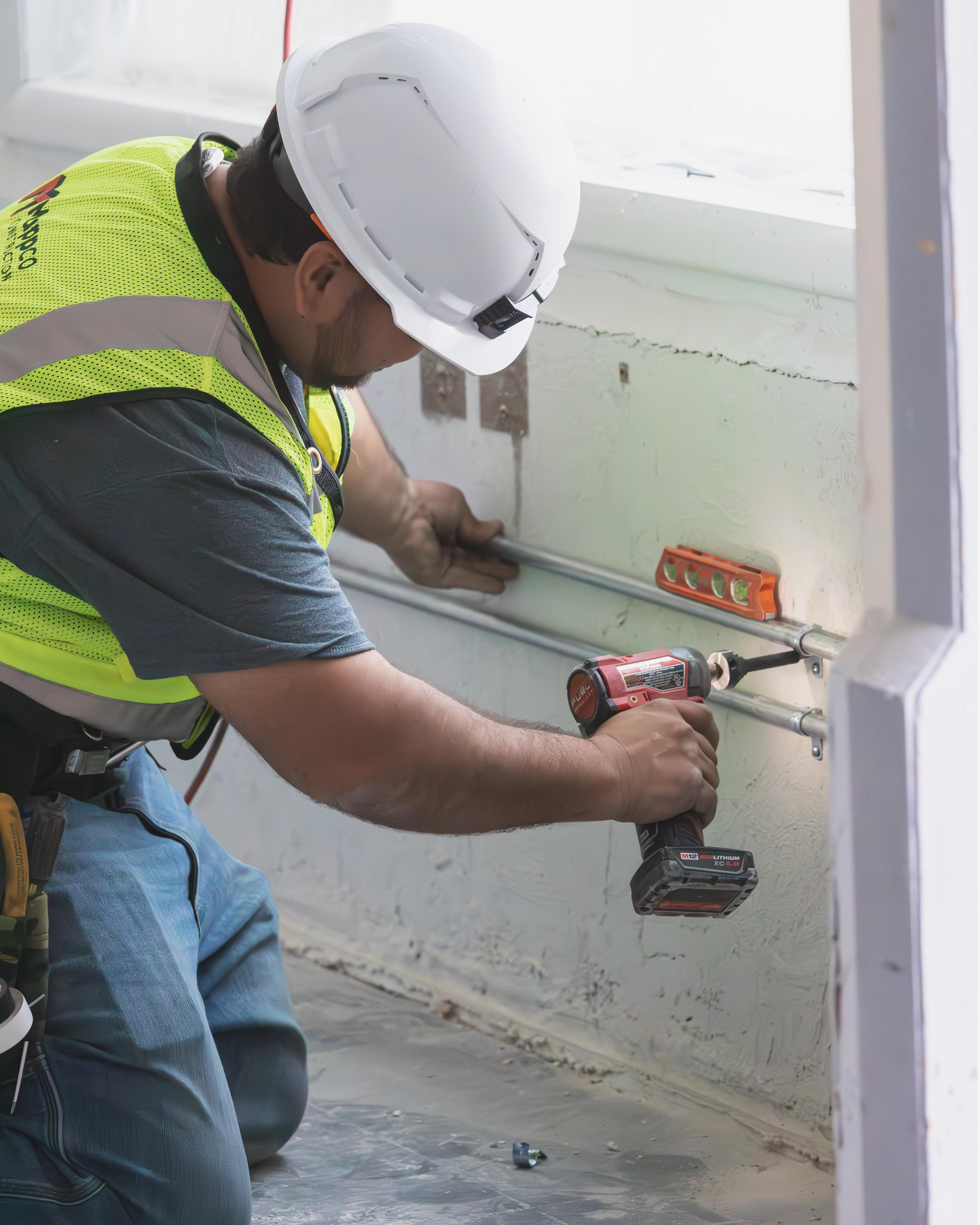 A Mappco Construction professional is diligently at work, focused on securing a component with a cordless drill on an active construction site.