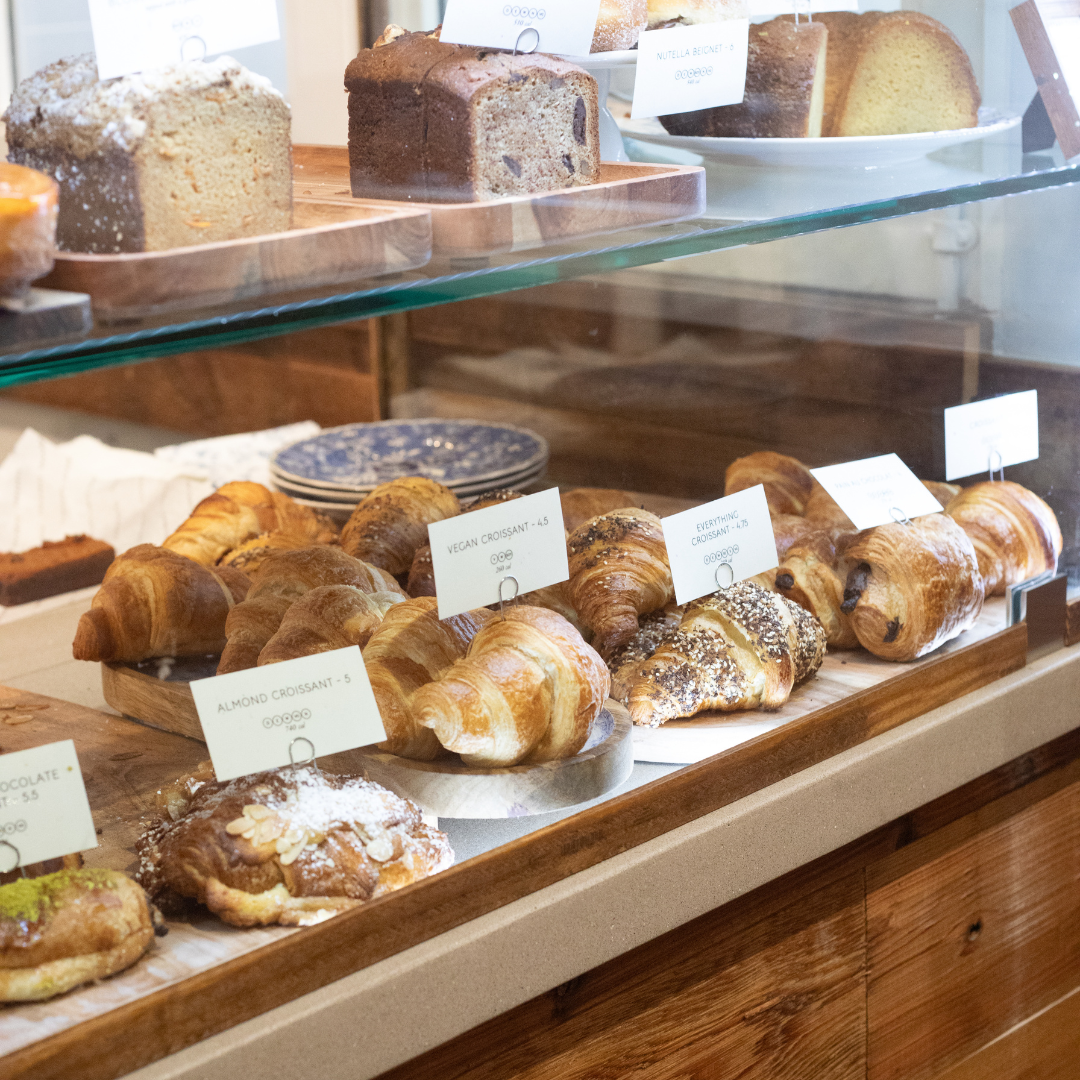 The image shows a display case filled with various baked goods, highlighting a selection of pastries 