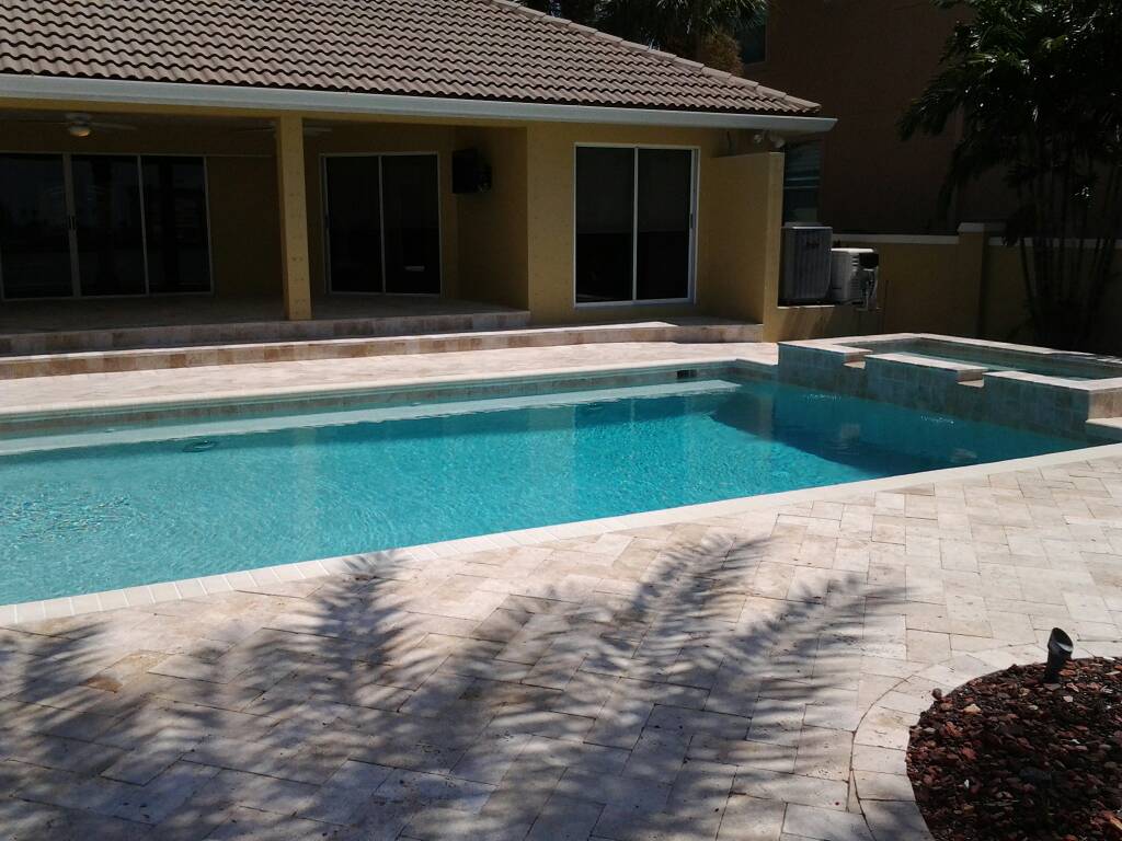 Backyard swimming pool with an integrated spa, light paver decking, and a covered patio beside the home.