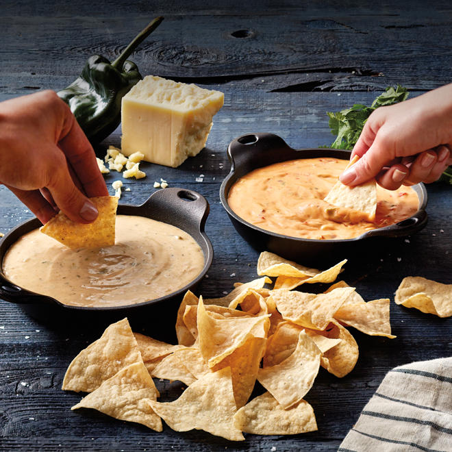 À gauche, une main trempe des chips dans un Queso 3 fromages de Quoba et une autre main sur la droite trempe des chips dans un Queso Diablo de Quoba avec une pile de chips au premier plan.