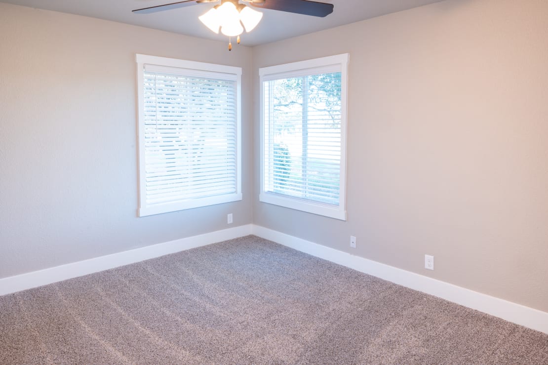an empty room with two windows and a ceiling fan