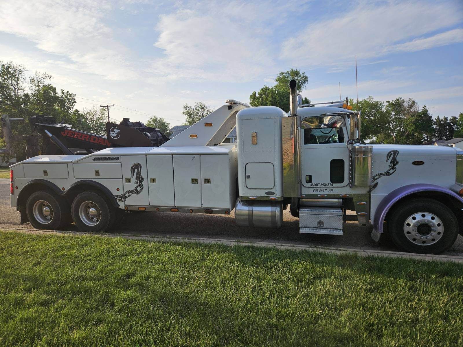 A side profile photo shows a white Peterbilt commercial tow truck equipped with a Jerr-Dan wrecker, parked beside a green lawn, featuring prominent chrome accents and black chain graphic decals.