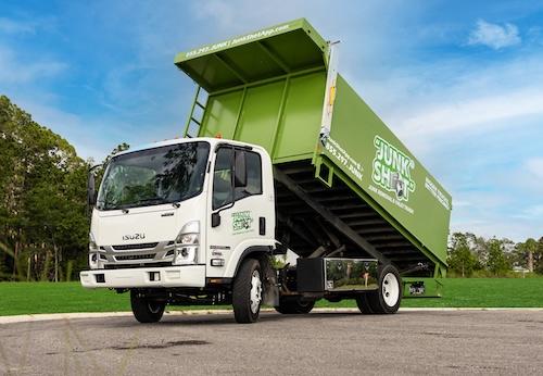 A three-quarter front view of a white Isuzu commercial truck with its large, green Junk Shot dumpste 