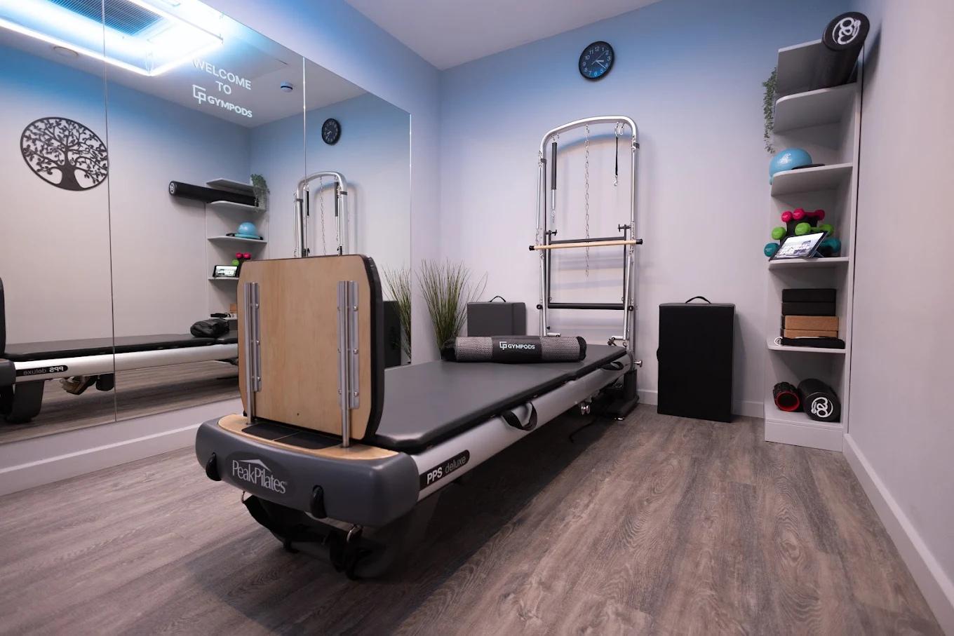 Private Pilates reformer studio at GYMPODS Putney with mirrored wall, reformer machine and neatly arranged training equipment.