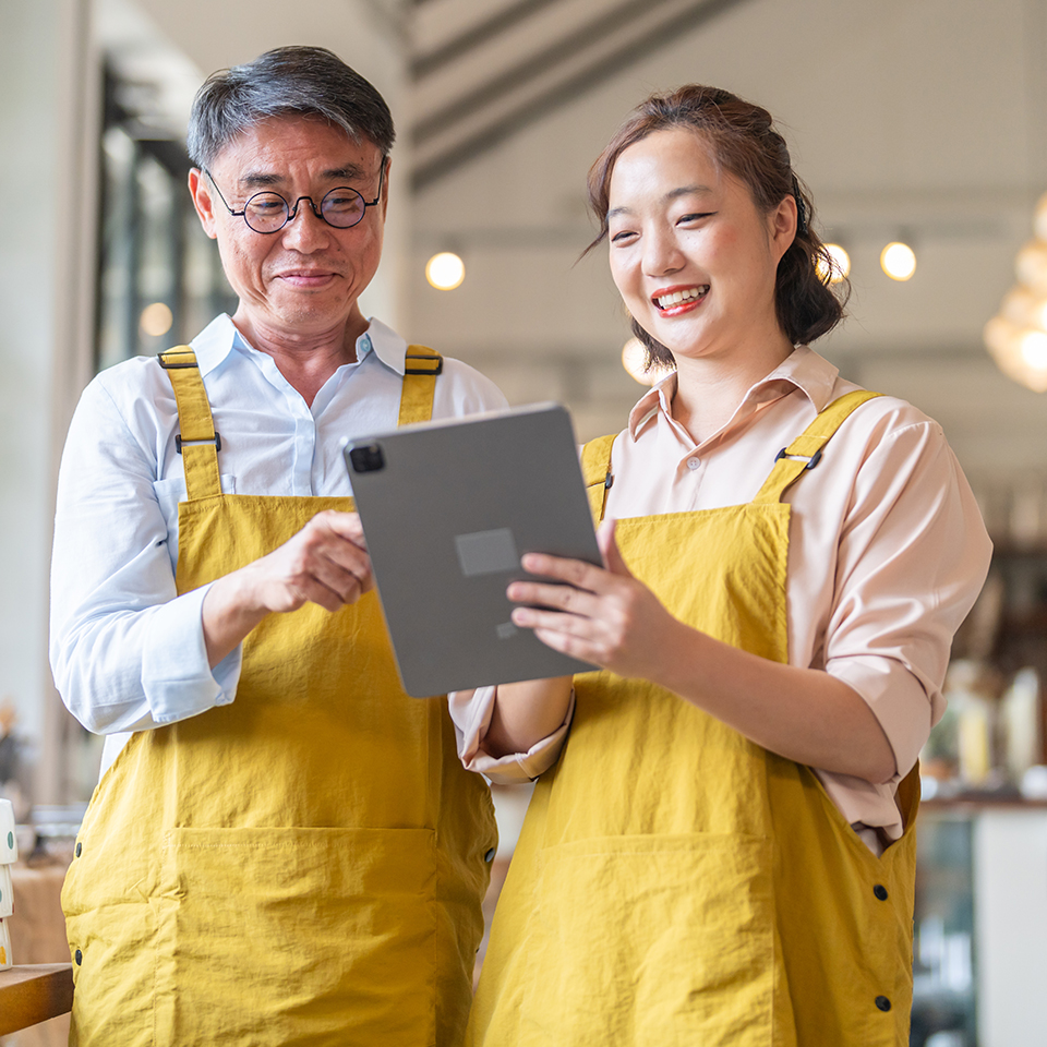 A man and woman in yellow overalls looking at a tablet.