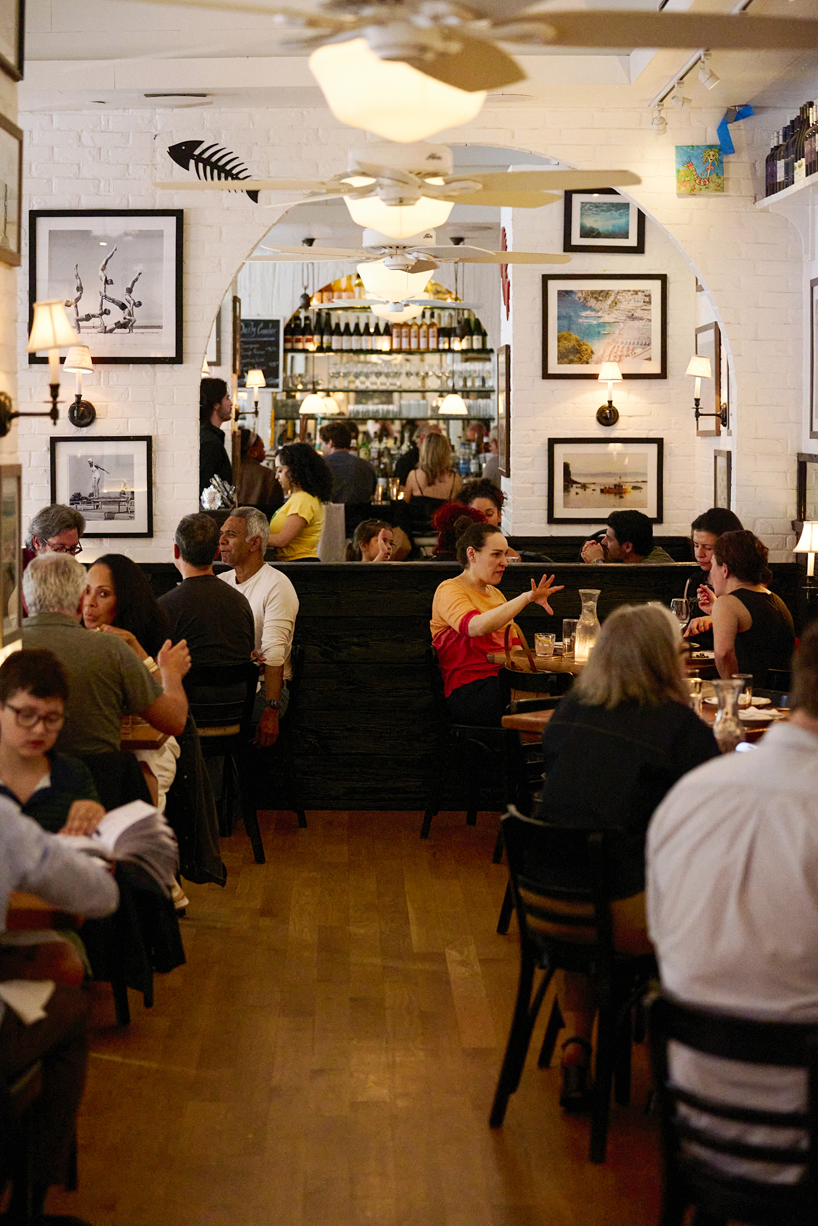 Step inside The Mermaid Inn — a lively dining room buzzing with energy. White-painted brick walls are adorned with framed coastal photography, creating an inviting, relaxed atmosphere. A neighborhood gem with the soul of a seaside escape.