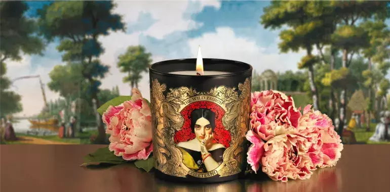 A captivating product visual generated by Tabula Rasa Social Stationers, showcasing the Coreterno "The Wild Passion" scented candle. The black candle vessel is elaborately decorated with intricate gold artwork and a central classical portrait, embodying the brand's unique blend of ancient traditions, modern design, and rebellious spirit. Flanked by lush pink peonies and set against a picturesque landscape backdrop, this image highlights the candle's ability to evoke deep emotions and transform any space into a sanctuary of style and mystery through its captivating aromas and bold design.