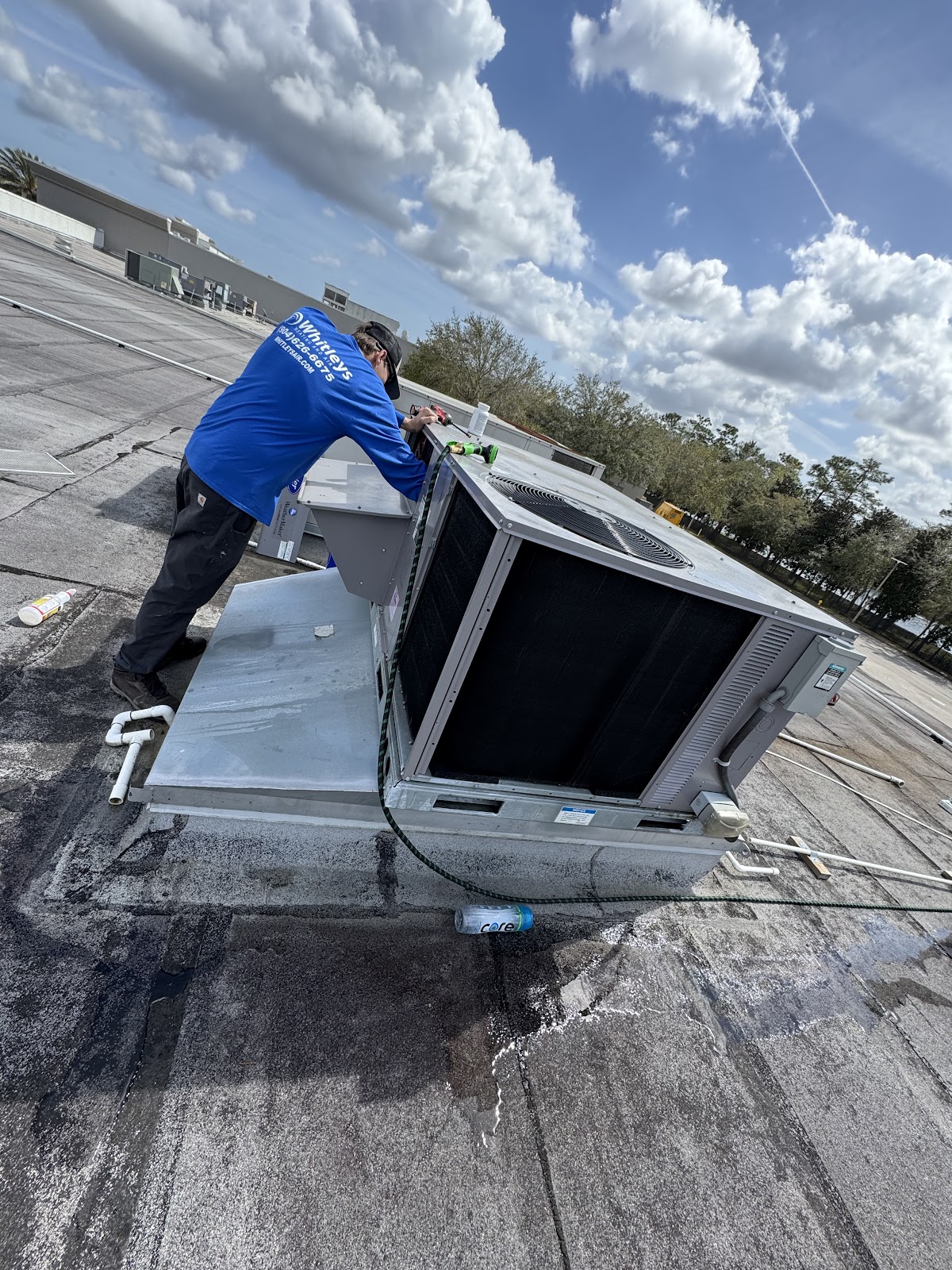 A person in a blue shirt with the Whitleys logo is working on an HVAC unit on a rooftop. The person  
