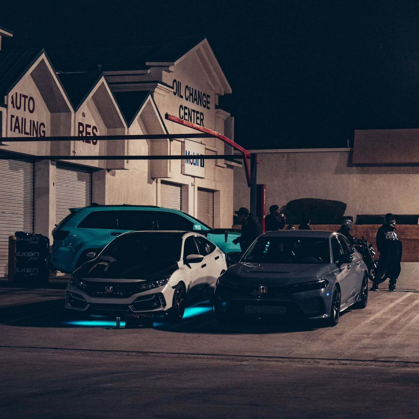 Two customized Honda Civic hatchbacks parked outside an automotive service center during a nighttime 