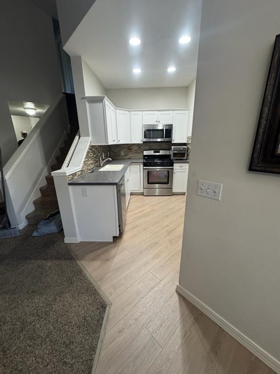 A modern kitchen with white cabinets, stainless steel appliances, and a tiled backsplash is visible. 