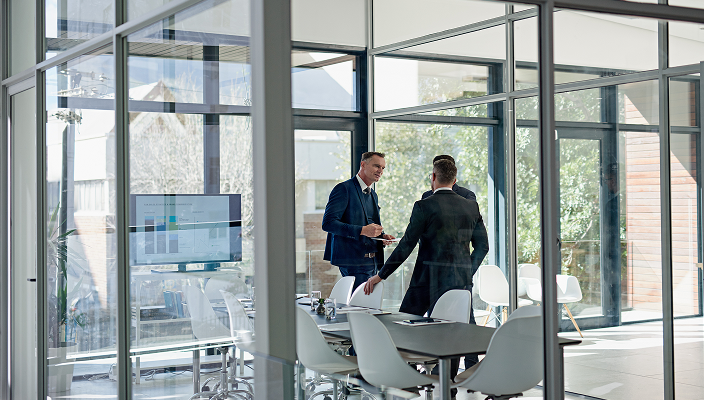 Three advisors meeting in a bright, glass-walled boardroom.
