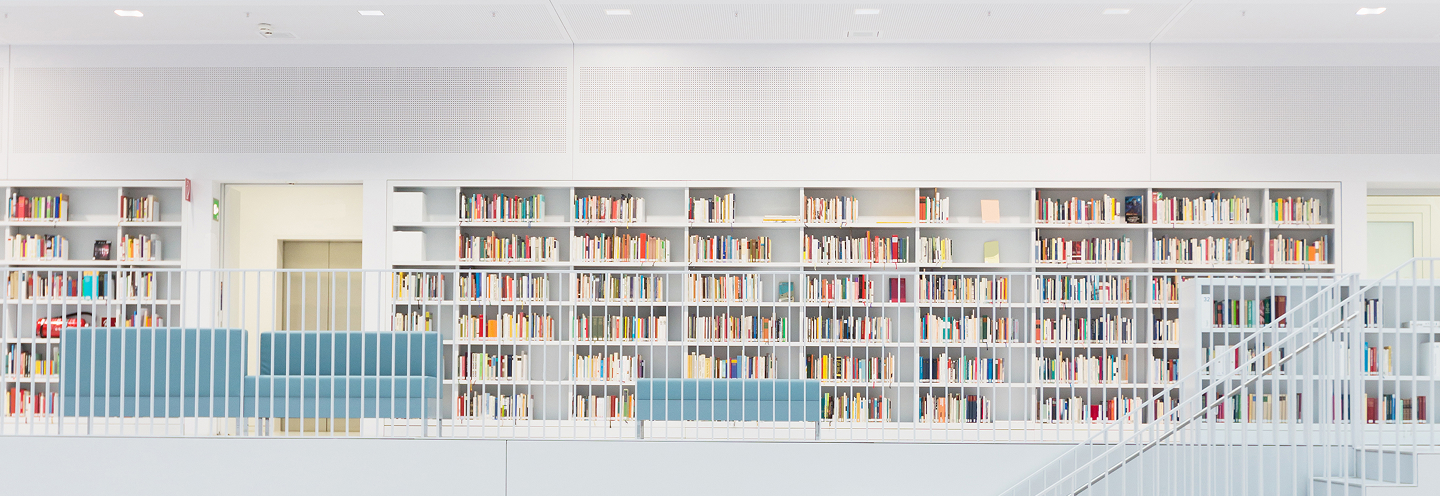The second floor of a white, modern library showcasing a row of bookshelves full of colourful books.