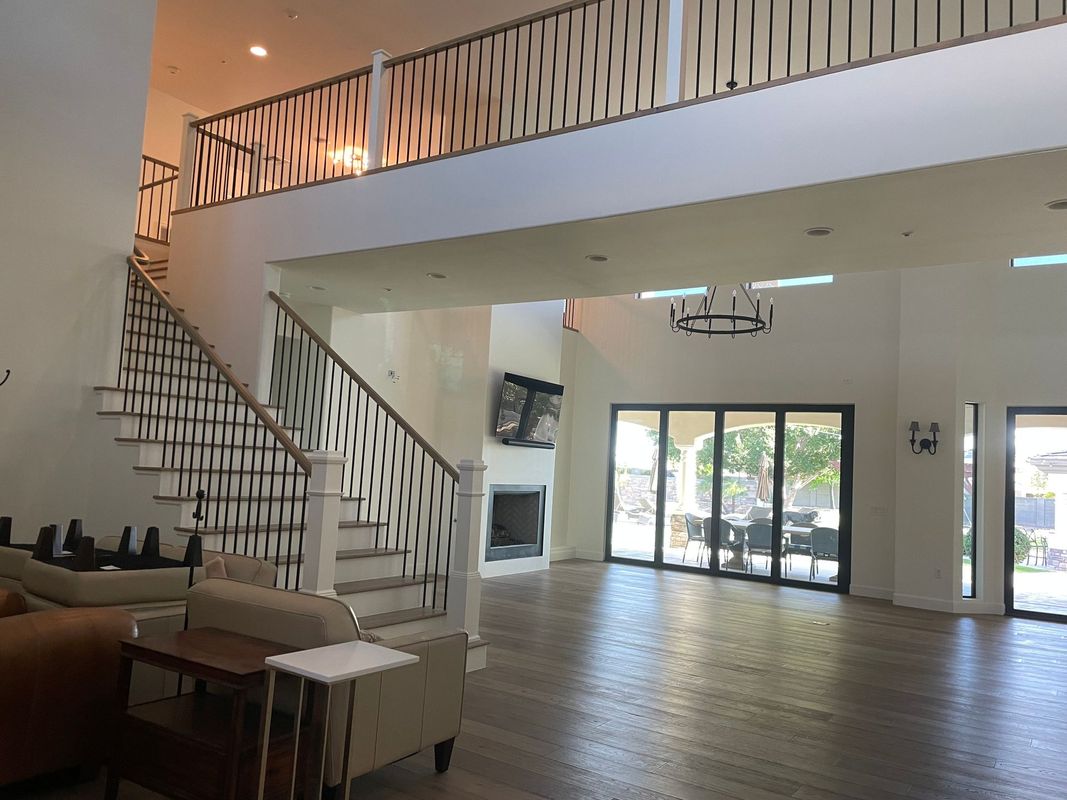 A spacious modern living area with high ceilings, staircase, balcony railing, fireplace, and large glass doors leading to an outdoor patio, featuring clean design and abundant natural light.