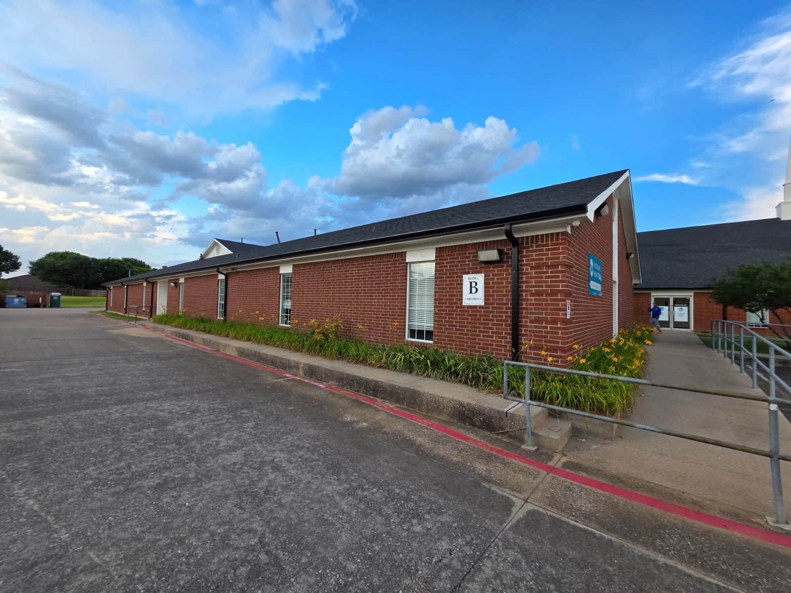 Commercial roofing project showing a long brick building with a dark shingle roof, landscaped surrou 
