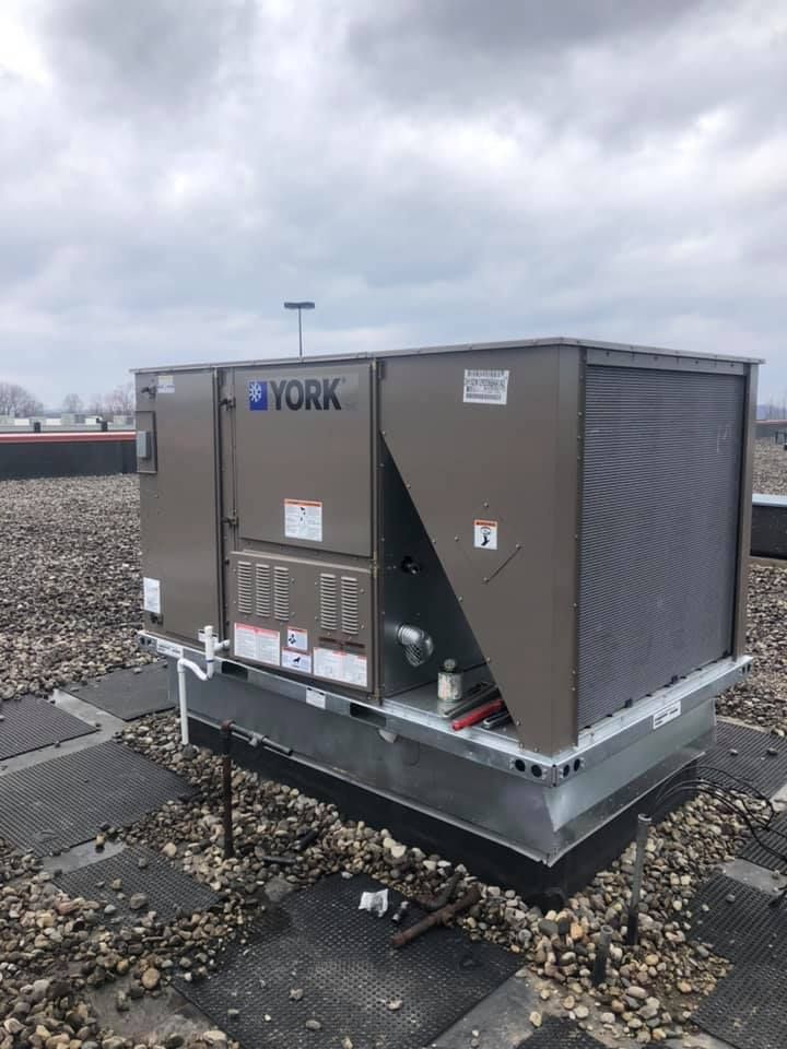 York rooftop HVAC unit installed on commercial building, mounted on raised platform with surrounding gravel surface, showing ventilation panels, piping connections, and professional setup for efficient heating and cooling system operation.