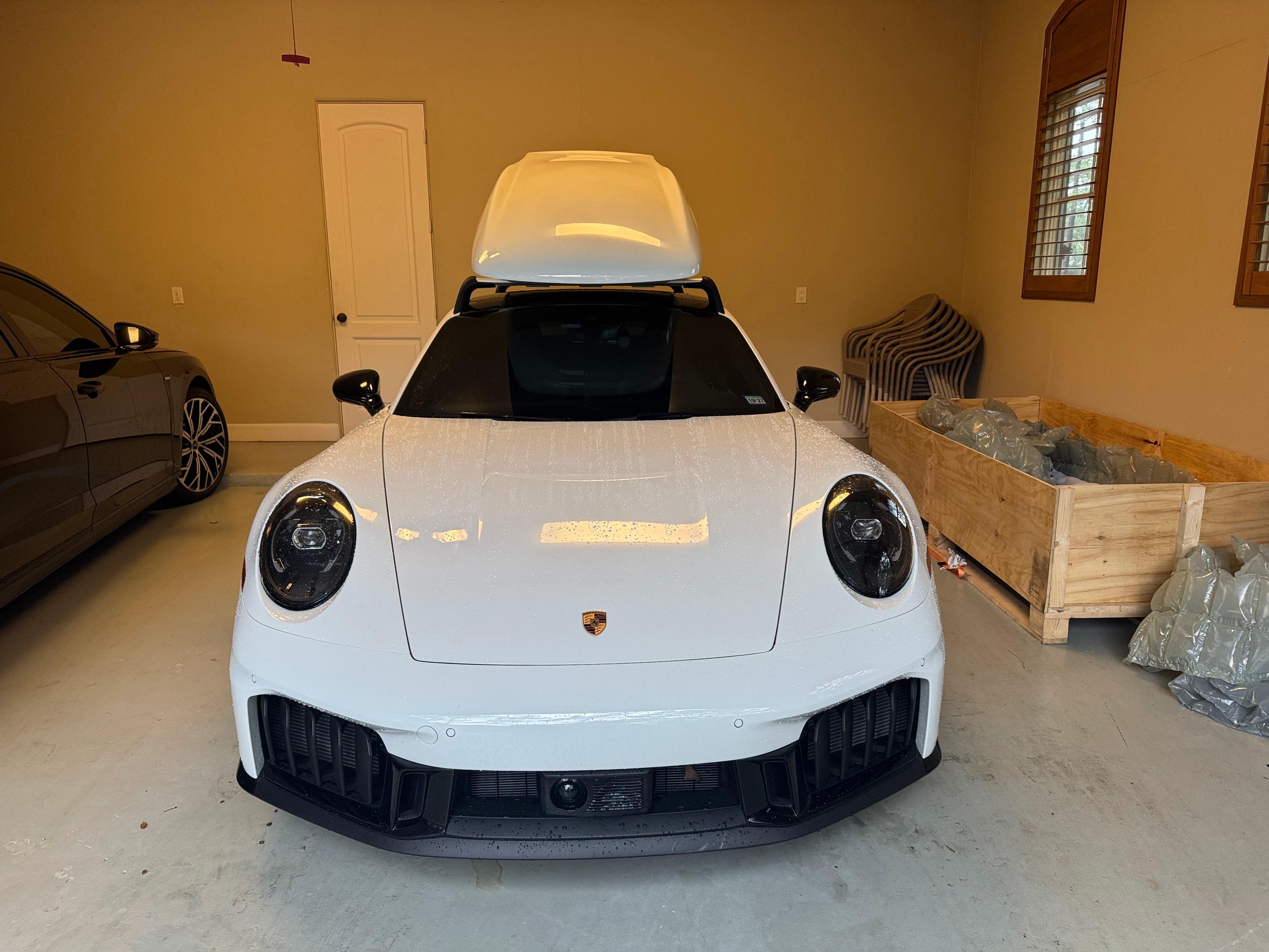 Porsche with a white roof cargo carrier mounted on top in a Houston garage.